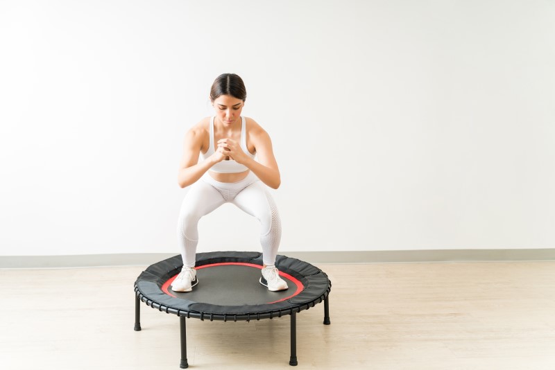 Frau in Squatposition auf Trampolin